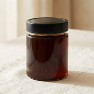 Pot en verre de miel de jujubier de 250 g, couvercle noir, posé sur un lin crème